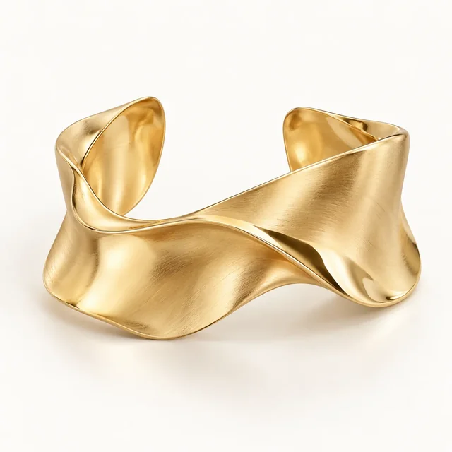An organic sculptural gold cuff on an ivory background
